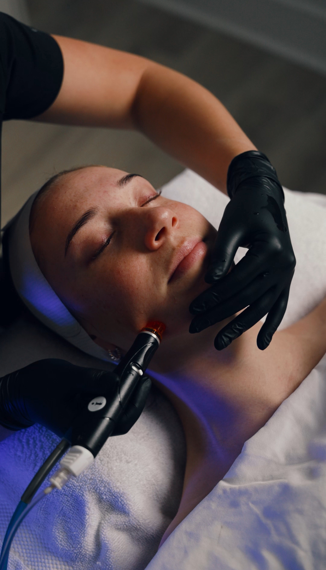 A person receiving a facial treatment with a device on their chin and blue light therapy.